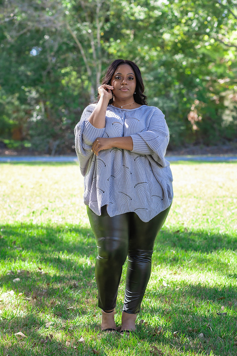 Shop Plus Sizes for Women Over 40 | Jolie Vaughan Boutique [Image Description: A stunning plus-size woman wearing a grey chunky knit sweater with a pair of faux-leather skinny pants from Jolie Vaughan Boutique.]