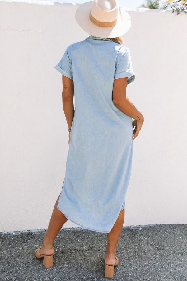 Woman wearing a casual Chambray Button-Up Midi Dress. Comfortable 100% cotton Chambray Midi Dress with button closure. Trendy Chambray Midi Dress with collared neckline and short sleeves. Side view of Chambray Midi Dress with side slits for comfort. Casual style Chambray Button-Up Midi Dress for everyday wear. Stylish Chambray Midi Dress, perfect for work or school. Woman dressed in Chambray Midi Dress with rolled-up sleeves.