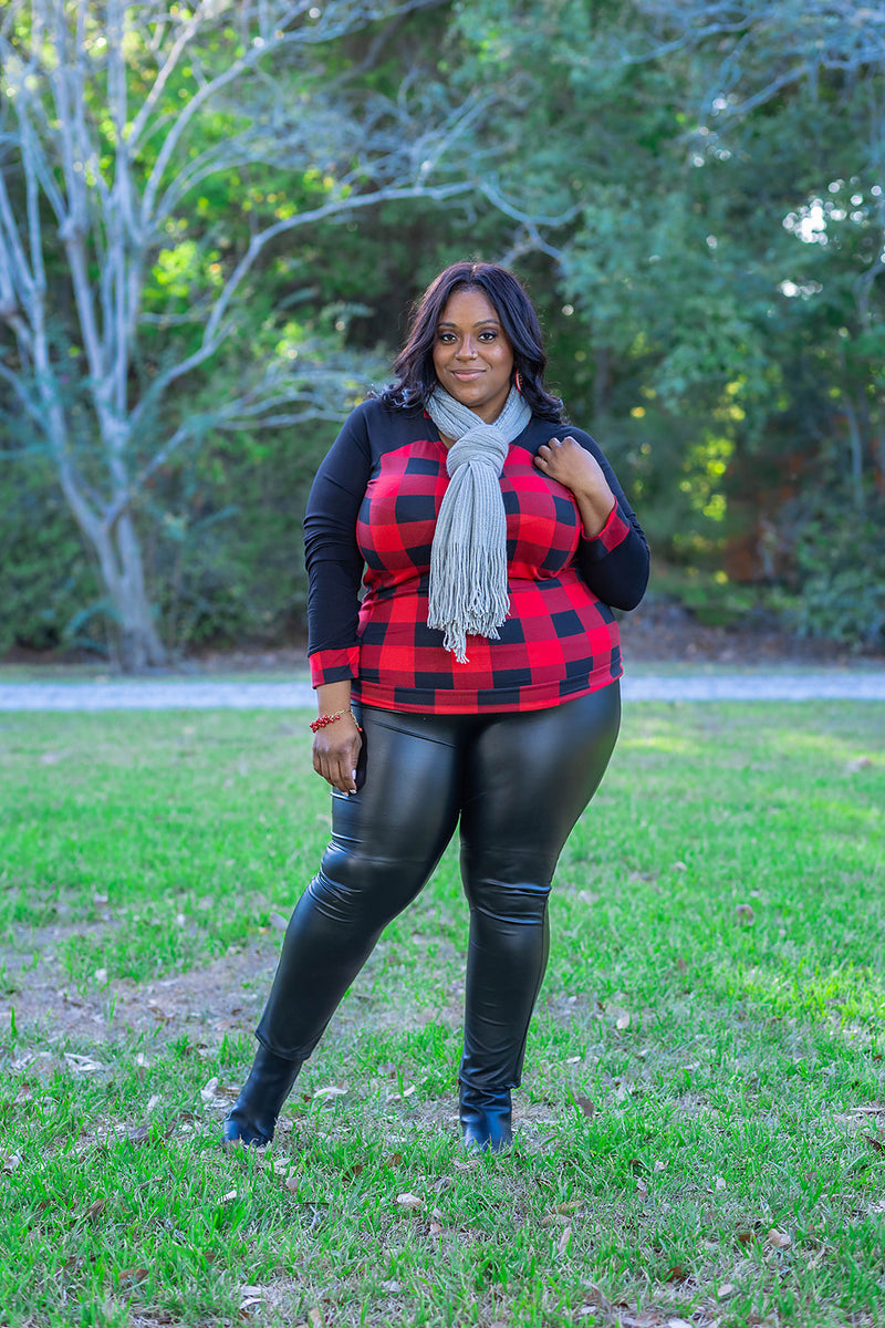 Raglan sleeve contrasting long sleeve top with red and black buffalo check print. This image features a gorgeous, plus size woman over 40 rocking this gingham print long sleeve crew neck top with a grey fringe scarf, red geometric earrings, and faux leather leggings with a pair of faux leather booties from the fall collection at Jolie Vaughan Boutique.