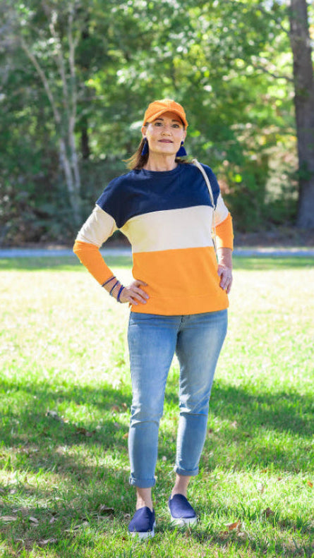 Woman wearing a colorful sweater and cap standing in a grassy area with trees in the background