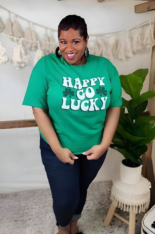 Smiling woman wearing a green St. Patrick's Day T-shirt with 'HAPPY GO LUCKY' text, styled with a black cardigan and blue jeans.